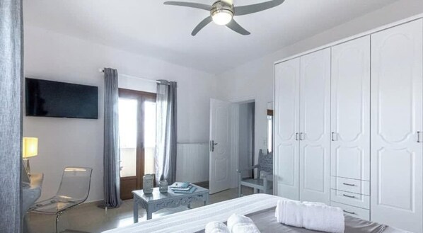 Una habitación de hotel con cama, escritorio, silla, armario y ventilador de techo.