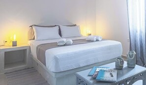 Un lit bien fait, avec des oreillers et une couverture, une table de chevet avec un livre et un vase, et une petite table de nuit avec une lampe.