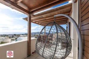 A balcony with a hanging net chair, wooden pergola, and a view of the cityscape.