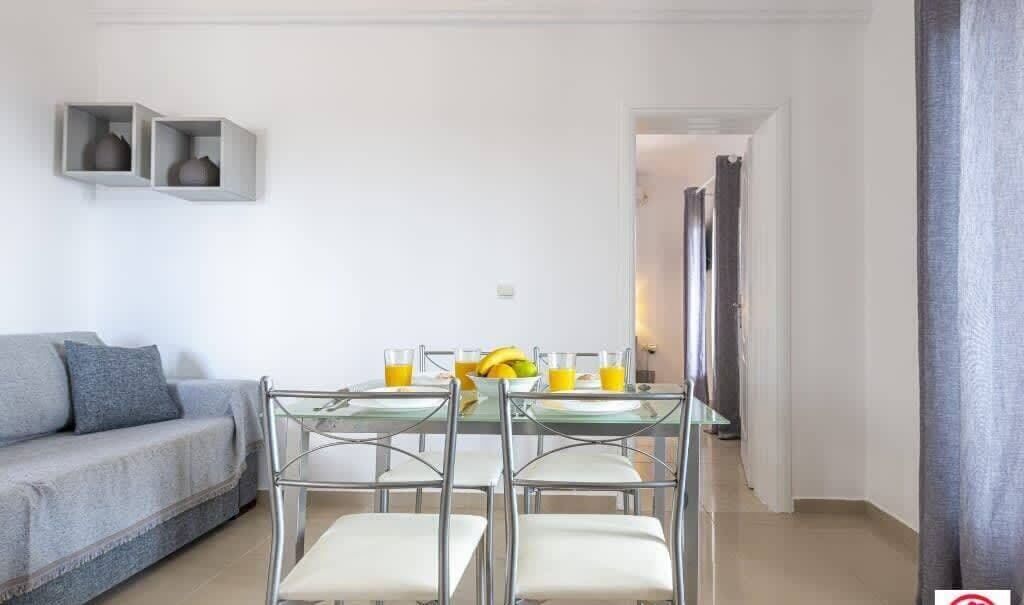 Ein modernes Wohnzimmer mit einer Couch, einem Esstisch mit Stühlen und einer Küche im Hintergrund.