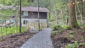 A cabin with a gravel path leading to it, surrounded by trees and a deck. - BearHaus1- Central Ac, Firepit, pool, gym (Killington)