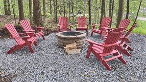 A circular fire pit surrounded by red Adirondack chairs in a forest setting. - BearHaus1- Central Ac, Firepit, pool, gym (Killington)