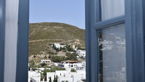 A view through a window of a coastal town with white buildings, a hill in the background, and a clear sky. - Relaxing Patmos Studio by the Aegean No 3 (Patmos)