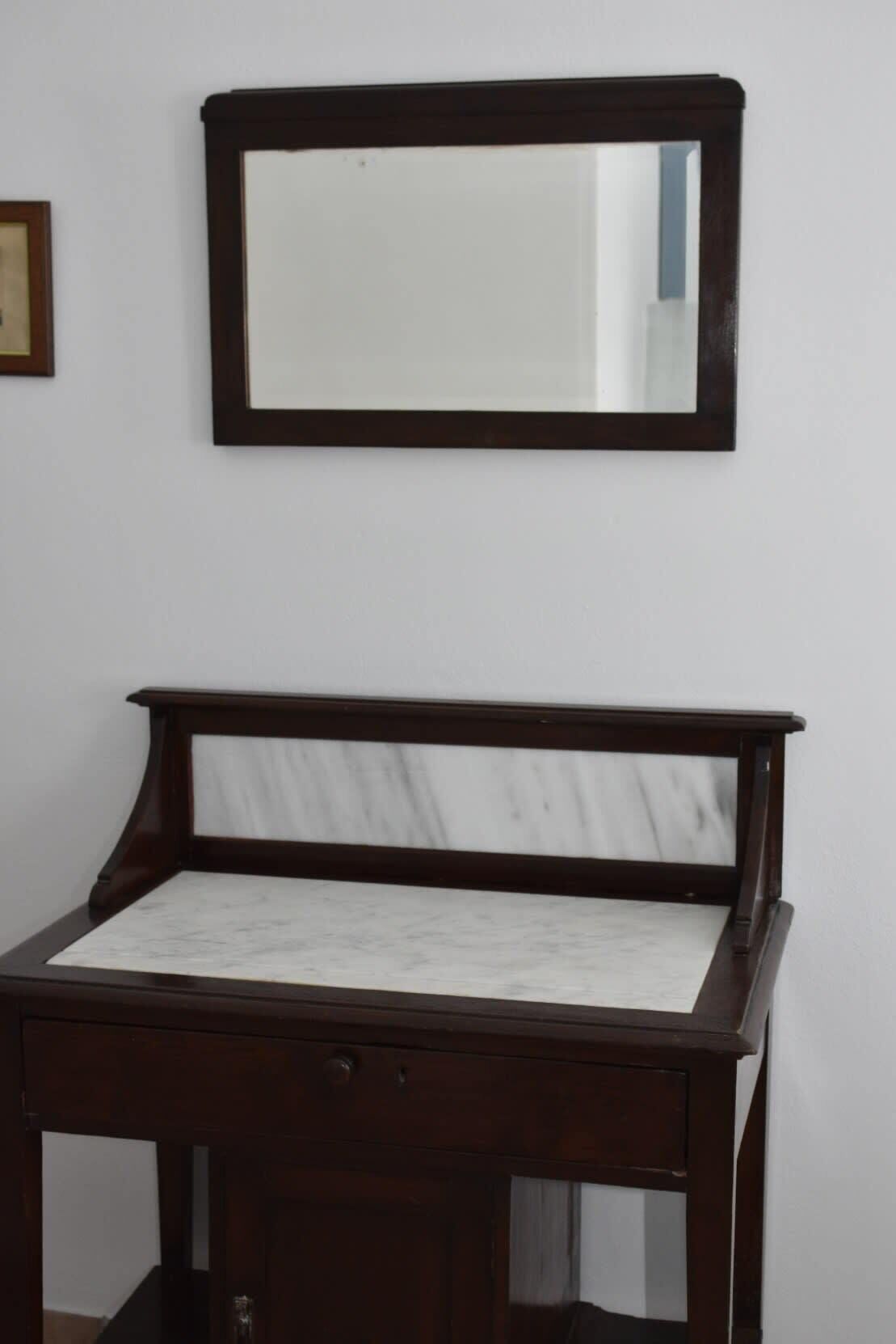 A dark wooden desk with a marble top and a mirror above it.