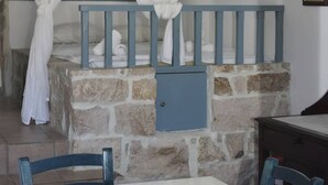 A bedroom with a stone wall, a bed with white linens, a blue headboard, and a window with white curtains. - Relaxing Patmos Studio by the Aegean No 2 (Patmos)