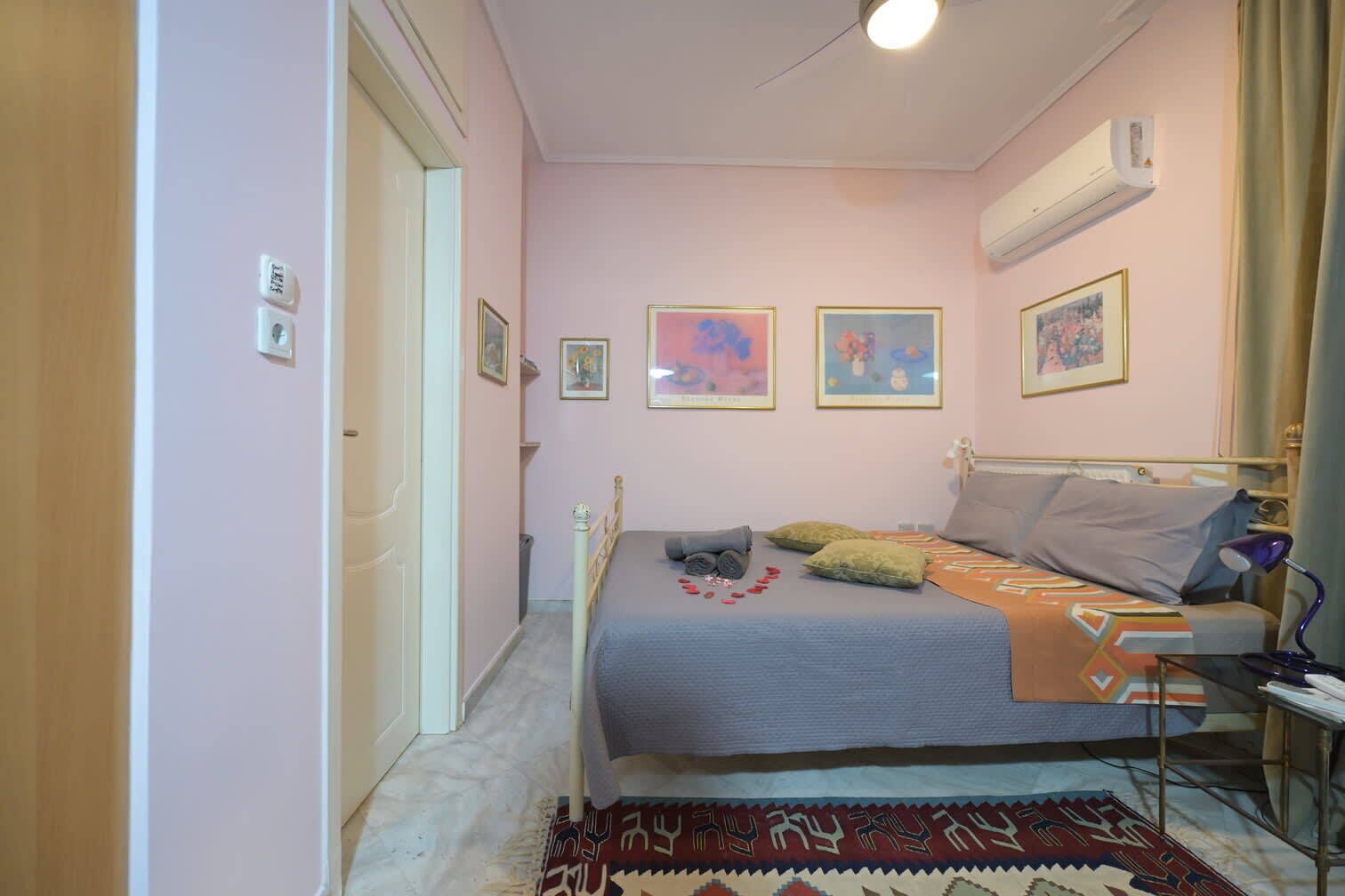 Een slaapkamer met een bed, een nachtkastje, een lamp en een wandairconditioner.