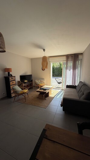 Een woonkamer met een bank, een televisie, een rieten stoel en een houten salontafel.