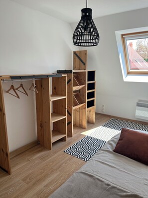 A room with a loft bed, wooden shelving, a hanging light fixture, and a window with a view of a brick building.