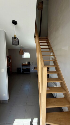 Un escalier avec des marches en bois et une rampe, menant à une pièce dont le sol est recouvert de carreaux et qui possède une fenêtre.