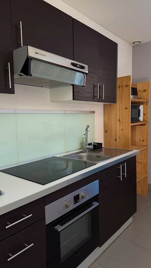 A modern kitchen with dark cabinetry, a stainless steel range hood, a built-in oven, and a microwave.