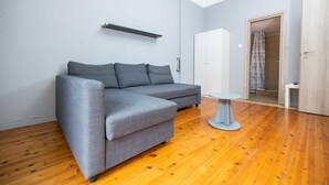 Een moderne woonkamer met een grijze hoekbank, een klein rond tafeltje en een kledingkast.
