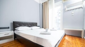 Een net opgemaakt bed met witte lakens en kussens, een houten vloer en een raam met gordijnen.