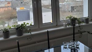 A room with large windows overlooking a cityscape, featuring potted plants and a table with candles and glasses. - Bright & Charming Studio at Alexanderplatz (Berlin)