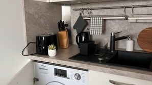A compact kitchen with a built-in washer and dryer, a coffee maker, a knife block, and a hanging pot rack. - Bright & Charming Studio at Alexanderplatz (Berlin)