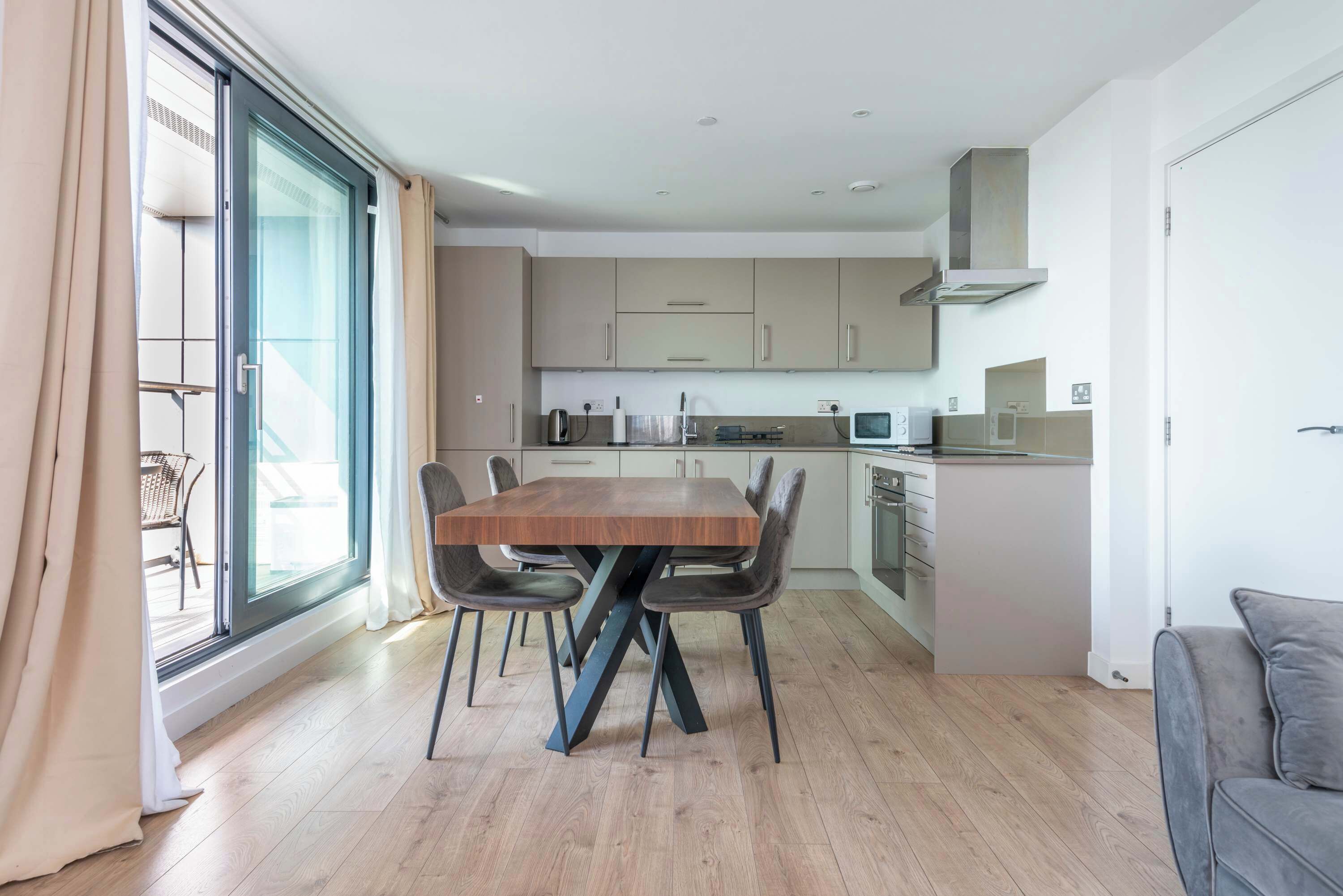 Una cocina moderna con una mesa de comedor y sillas, horno empotrado y un gran ventanal con cortinas.