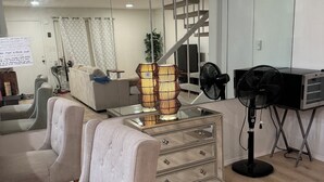 Een moderne woonkamer met een bank, een glazen salontafel, een decoratieve lamp, een ventilator en een trap.