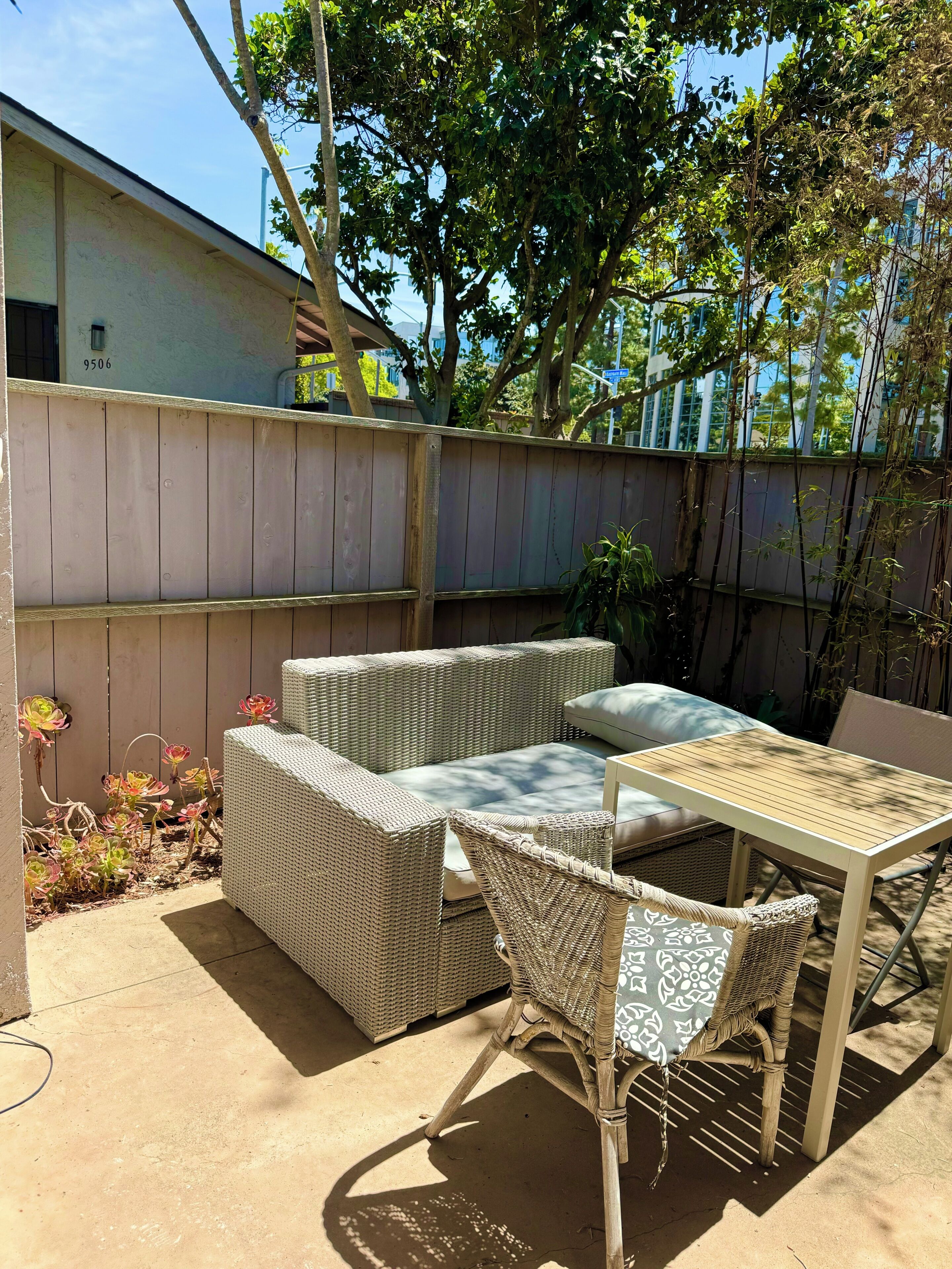 Une terrasse dotée de meubles en osier, d’une table et offrant une vue sur un bâtiment en arrière-plan.
