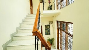 A staircase with wooden handrails and white steps, leading to a landing with a potted plant and a framed picture. - BedChambers Serviced Apartments -Artemis (Gurugram)