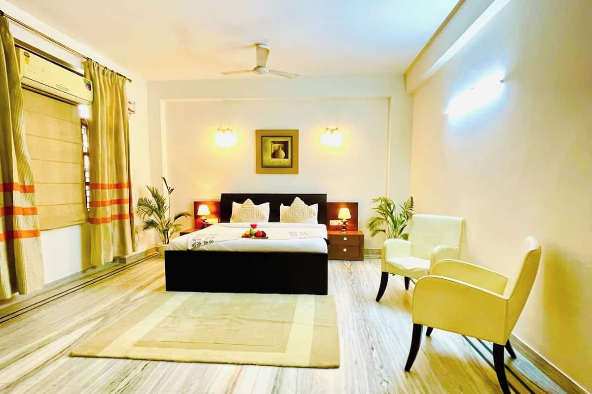 Habitación de hotel con cama, ventilador de techo, mesita de noche, una silla y un ventanal con cortinas.