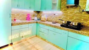 A kitchen with teal cabinets, granite countertops, and a gas stove. - BedChambers Serviced Apartments -Artemis (Gurugram)