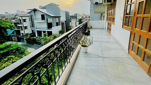A balcony with a view of neighboring buildings, a potted plant, and a window with a wooden frame. - BedChambers Serviced Apartments -Artemis (Gurugram)