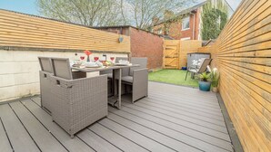 Une terrasse dotée de meubles en osier, une table mise avec des verres à vin et, en arrière-plan, un mur de briques.