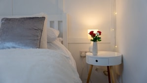 Un lit bien fait, avec un oreiller moelleux et une table de chevet ornée d’un vase de fleurs.
