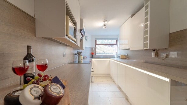 Une cuisine moderne avec des meubles blancs, un plan de travail en bois et une vue sur le salon attenant.
