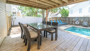 Eine überdachte Terrass mit Glastisch und Korbstühlen, einem Pool und einem Holzboden.