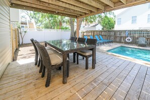 Un patio cubierto con una mesa de vidrio y sillas de mimbre, una piscina y una terraza de madera.