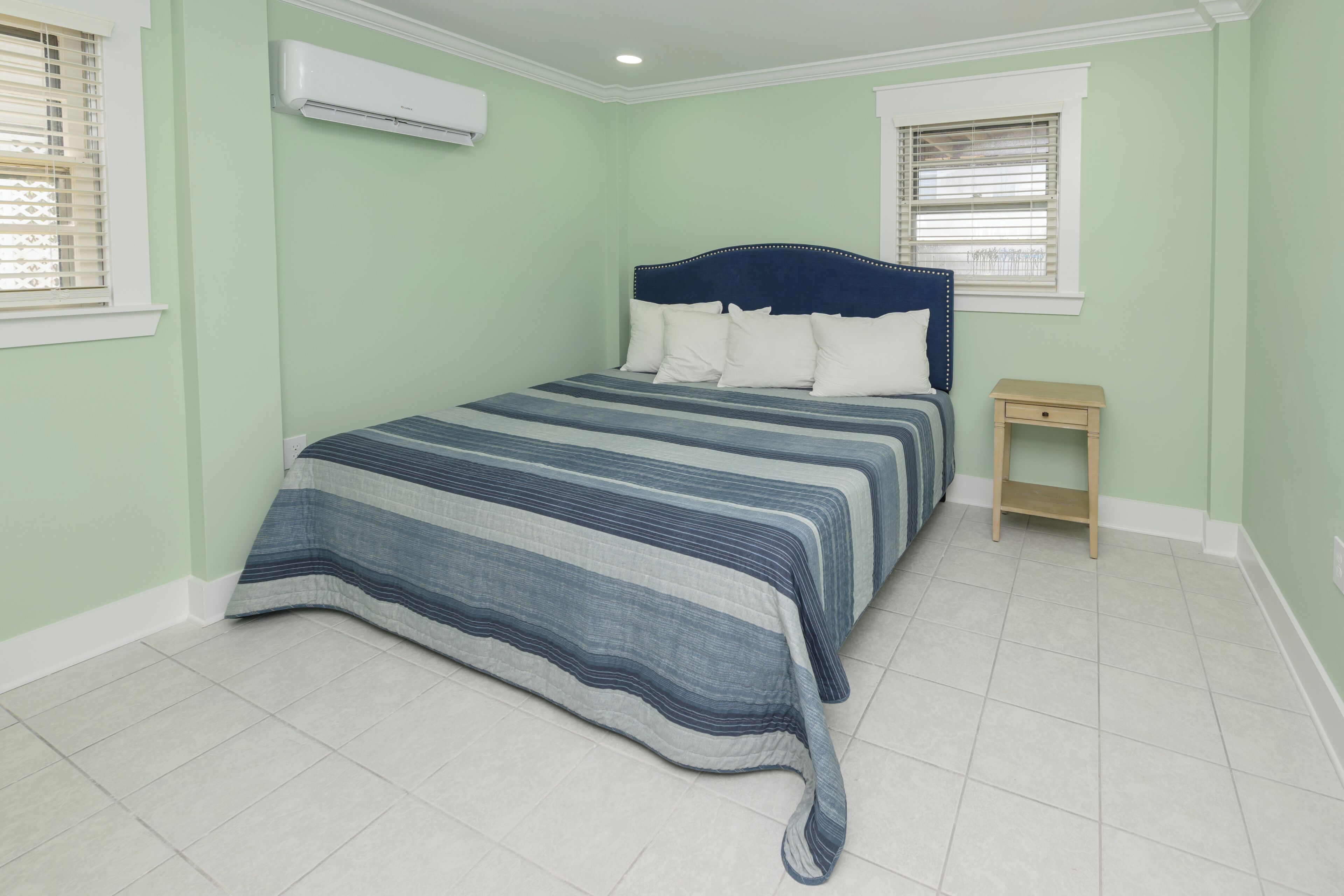 A bedroom with a bed, a nightstand, and an air conditioning unit.