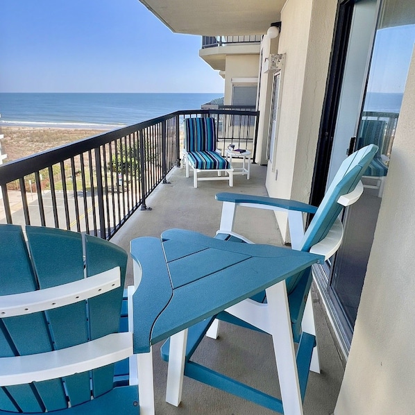 A balcony with a view of the ocean, featuring two chairs and a table.