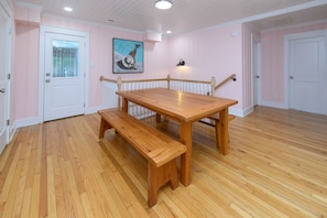 Une pièce avec une table et un banc en bois, une porte blanche et un tableau représentant une scène de baignade.