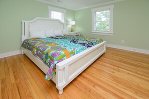 A bed with a colorful bedspread, a white headboard, and a nightstand with a lamp.