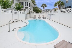 Une piscine dotée d’une terrasse blanche, d’une échelle en métal et de deux chaises longues.