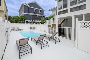 A backyard with a swimming pool, lounge chairs, a white fence, and a two-story house.