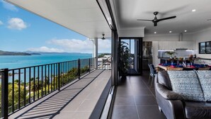 A balcony with a view of the sea, a dining area with a table set for two, and a modern kitchen. - Panorama at Shute Harbour (Shute Harbour)
