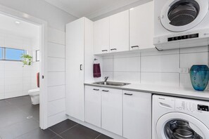 Une cuisine moderne avec des meubles blancs, un lave-linge encastré et une fenêtre agrémentée d’une plante.
