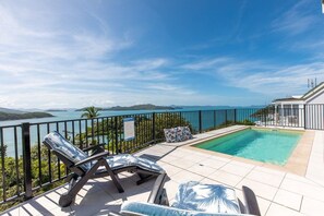 Un espace piscine avec des chaises longues, une vue sur la mer et un balcon grillagé.