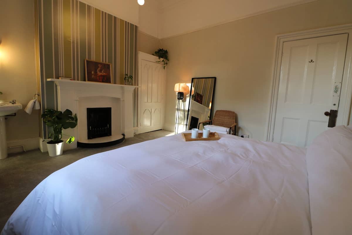 A bedroom with a large bed, a fireplace, a chair, and a door.