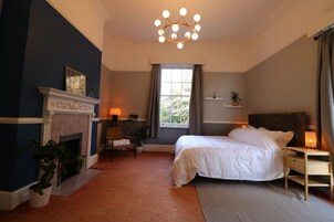 A bedroom with a fireplace, a bed, a nightstand, a chair, and a chandelier.