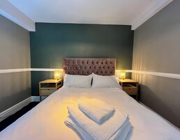 A neatly made bed with a tufted headboard, two bedside tables with lamps, and a stack of towels on the bed.