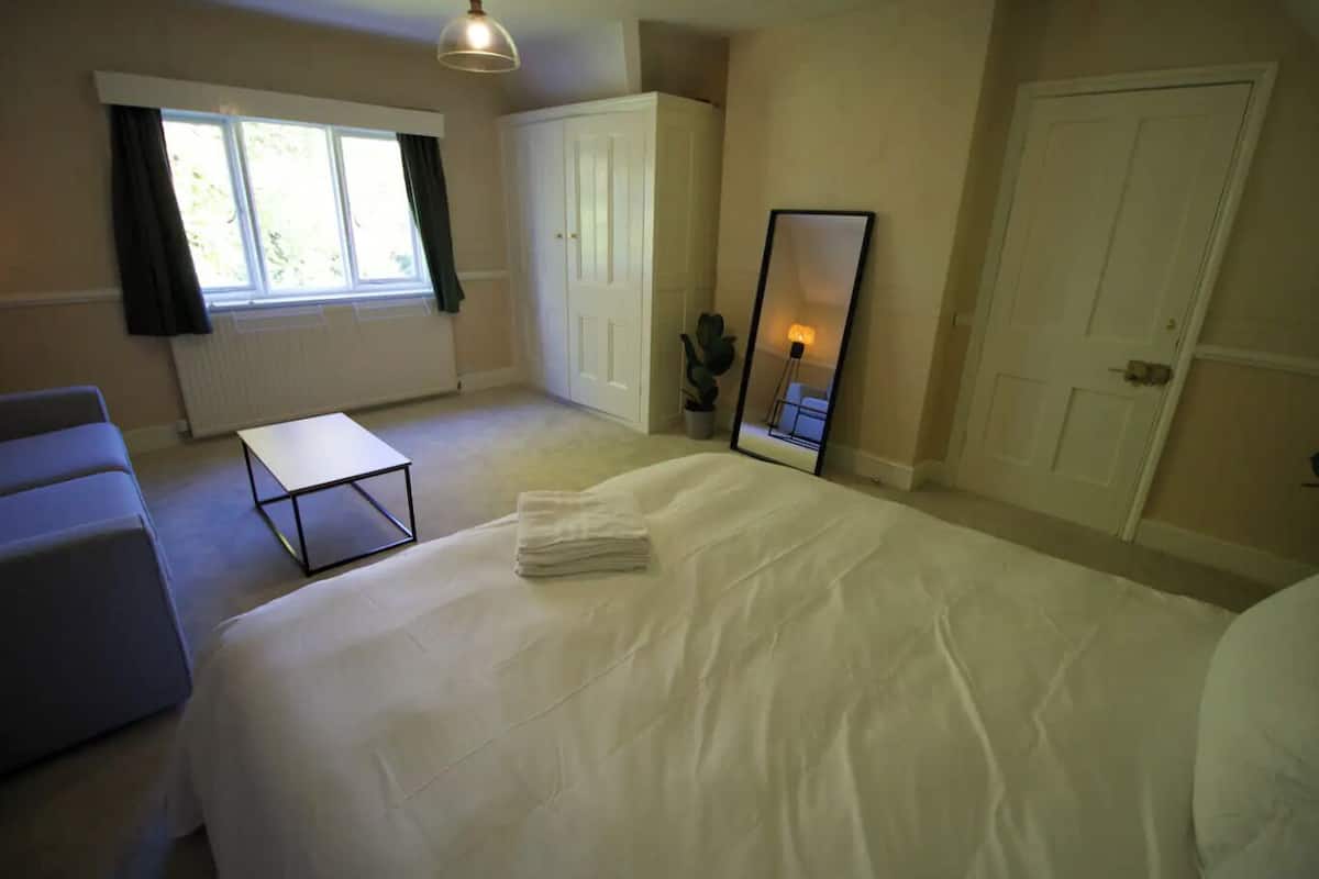 A bedroom with a bed, a small table, a chair, a window, and a mirror.