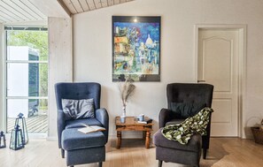 Quarto com duas poltronas, uma mesa de madeira pequena, um quadro na parede e uma porta.