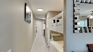 Una habitación de hotel con piso de madera, cama con ropa blanca, espejo de diseño único y ventilador de techo.