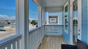 A covered porch with a wooden deck, white railings, and a wicker chair. - The Blue Pearls - Luxe Home, Close to Beach + Gulf Views! (Panama City Beach)