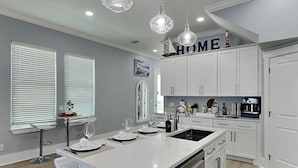 A modern kitchen with white cabinetry, a central island, and pendant lighting. - The Blue Pearls - Luxe Home, Close to Beach + Gulf Views! (Panama City Beach)