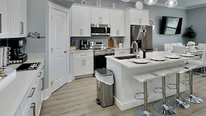 A modern kitchen with white cabinetry, stainless steel appliances, a central island with bar stools, and pendant lighting. - The Blue Pearls - Luxe Home, Close to Beach + Gulf Views! (Panama City Beach)