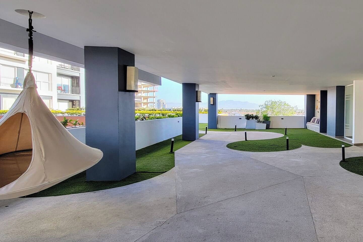 A modern outdoor area with hanging chairs, a concrete pathway, and a view of buildings in the background.