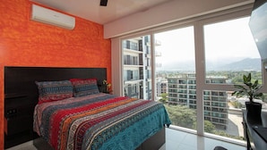 Een slaapkamer met een groot bed, een plafondventilator en uitzicht op een stadsgezicht door een groot raam.